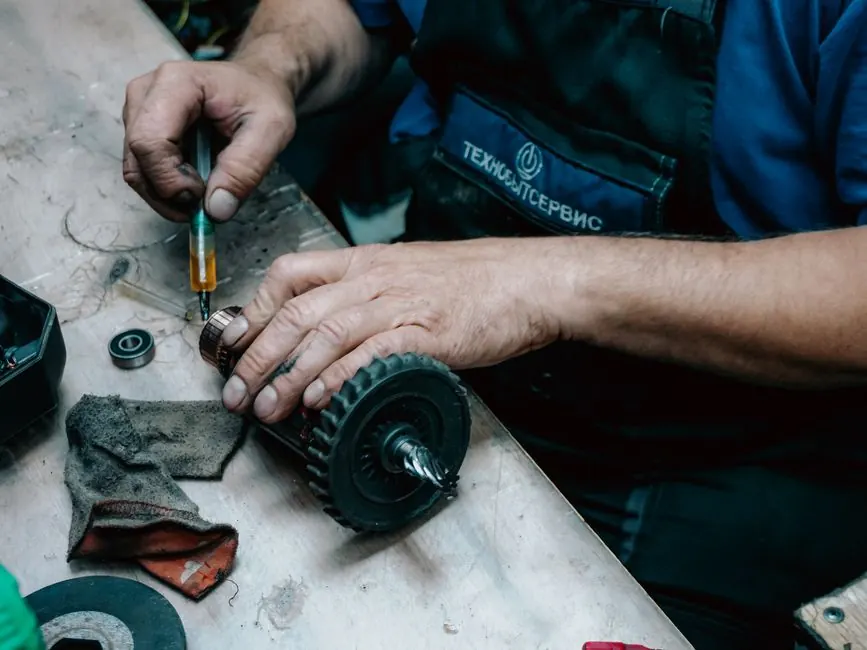 Detailed view of a technician working on a mechanical gear part with precision tools on a workbench.